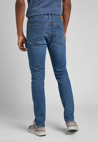 Niebieskie dżinsy o slim fit, z jasnym praniem, delikatnym przecieraniem i skórzaną metką na tylnej części pasa. W zestawie z trampkami.