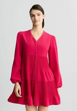 Short pink dress made of smooth fabric with long sleeves, a V-neck, vertical pleats, and decorative button accents down the front.