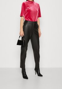 Haut en velours rouge à manches courtes, pantalon en cuir noir et bottines à talons hauts noires. Petit sac à main noir avec une bandoulière.