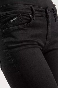 Czarne jeansy z denimu w slim fit, z przednimi kieszeniami i subtelnym logo na pasku. Tekstura jest gładka z lekkim połyskiem.