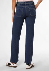 Tmavě modré džínové kalhoty s rovnýma nohavicema, viditelnými zadními kapsami, lemovaným okrajem a nošené s bílými teniskami s černými pruhy.