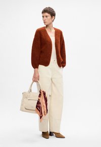 Rustfarvet, fluffy cardigan med en afslappet pasform, parret med cremefarvede wide-leg bukser og en beige håndtaske prydet med et mønstret silkebånd.