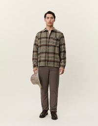Καρό φανελένιο πουκάμισο σε γήινες αποχρώσεις, φαρδιά εφαρμογή, με μία τσέπη στο στήθος; σε συνδυασμό με γκρίζες παντελόνες και μπεζ καπέλο. Τα σκούρα παπούτσια ολοκληρώνουν την εμφάνιση.
