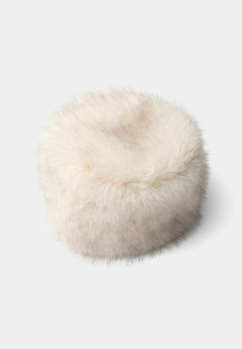 Runder Pouf aus weichem, hellbeigem Kunstfell. Plüschige Textur mit leichtem Glanz, präsentiert sich in einem nahtlosen Design und abgerundeten Kanten für ein gemütliches Erscheinungsbild.