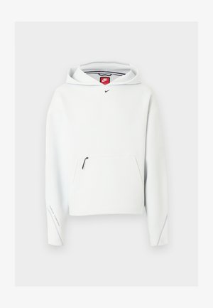 Bela Nike jopa s sprednjim žepom z zadrgo, majhnim črnim logotipom Nike na prsih in kapuco, prikazana na svetli ozadju.