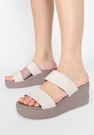 Jasno beżowe sandały na koturnie z dwiema szerokimi paskami i masywną podeszwą. Miękki materiał, gładka tekstura oraz profilowana wkładka dla komfortu.