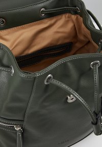 Sac seau en cuir vert foncé avec une texture douce, intérieur doublé en beige clair, fermeture à cordon, et accents en métal argenté.