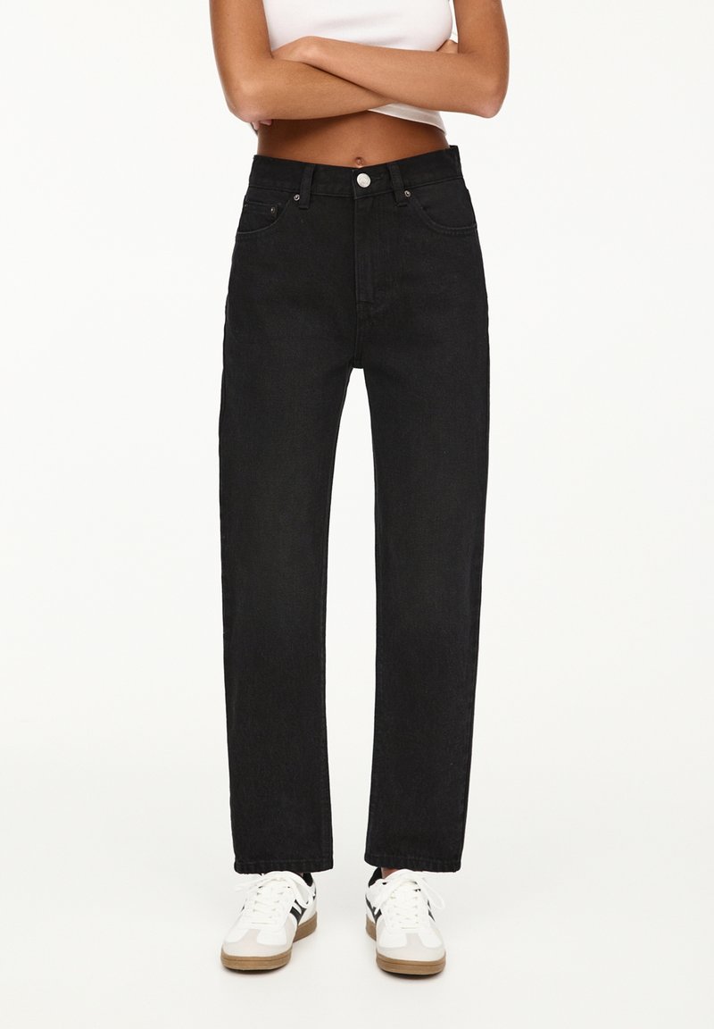 Black denim jeans with a straight leg design, featuring front pockets, a button closure, and subtle texture. Paired with white sneakers.