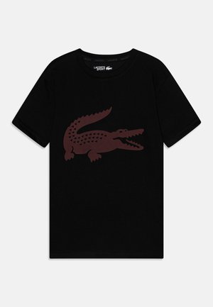 Czarny T-shirt z krótkim rękawem, z dużą ciemnobrązową grafiką krokodyla na środku przodu, metka Lacoste Sport wewnątrz kołnierza.
