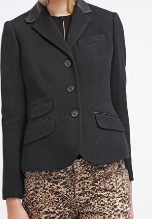 Blazer noir ajusté avec trois boutons et poches à rabat, porté avec un pantalon taille haute à imprimé léopard.