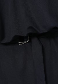 Gros plan d'une ceinture en tissu noir fixée avec une petite boucle en D argentée sur un vêtement noir assorti.