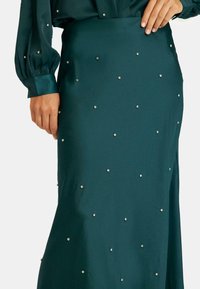 Falda de satén verde esmeralda con rhinestones decorativos dispersos, textura suave y un corte ajustado con un ligero brillo.