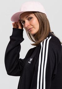 Hanorac negru cu dungi albe pe mâneci, având logo-ul Adidas; capac roz deschis; textură netedă, îmbrăcăminte sport casual.