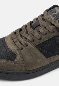 Sneaker con un mix di pelle verde oliva testurizzata e suede nero, lacci tondi marroni e suola in gomma con logo del marchio.