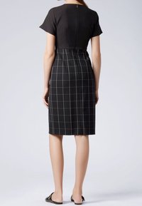Černé šaty s krátkými rukávy, strukturovaným korzetem a přiléhavou sukní se vzorem bílého mřížkování. Viditelné zapínání na zip na zadní straně.