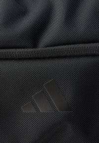 Musta pintakuvioitu kangas, jossa on sileä vetoketjullinen osa ja kohotettu musta logo, jossa on kolme vinoviivaa.