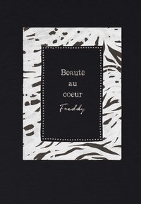 Tessuto nero con un pannello centrale bianco caratterizzato da un motivo animale testurizzato. Il testo recita "Beauté au cœur" e "Freddy", bordato da borchie argento.