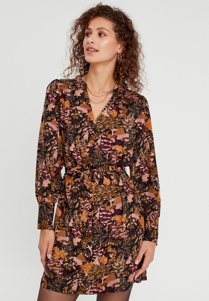 Robe à motifs floraux aux tons terreux, avec un décolleté en V, des manches longues et une taille nouée. Fabriquée en tissu léger avec une texture lisse.