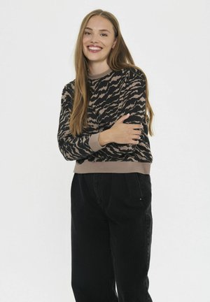 Pull en tricot avec un motif abstrait noir et beige, poignets et ourlet côtelés, associé à un pantalon noir taille haute. Texture douce.