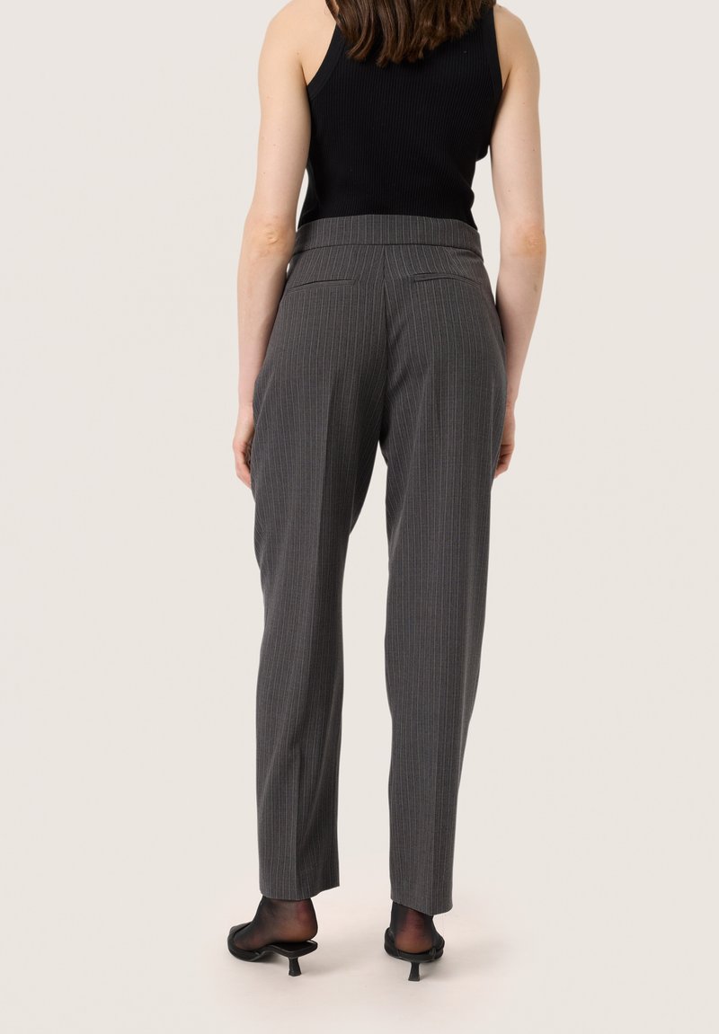Pantalons gris à rayures avec une coupe ajustée, taille mi-haute, poches arrière et texture lisse. Portés avec des chaussures à talons noirs.