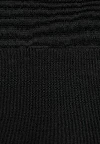 Gros plan sur un tissu noir présentant deux textures de tricot distinctes : un motif côtelé horizontal en haut et un tricot plus fin et serré en dessous.