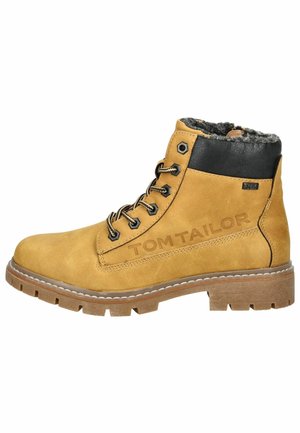 Bottines en suède marron avec des accents en cuir noir, doublure texturée, cinq œillets en métal et une semelle en caoutchouc chunky. Présente un logo en relief.