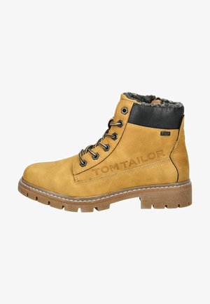 Bottines en suède marron avec des accents en cuir noir, doublure texturée, cinq œillets en métal et une semelle en caoutchouc chunky. Présente un logo en relief.