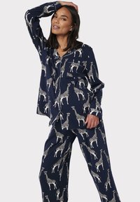 Navy pyjamastel gemaakt van zachte stof met een girafpatroon. Inclusief een overhemd met knopen en een zak, en bijpassende loszittende broek.