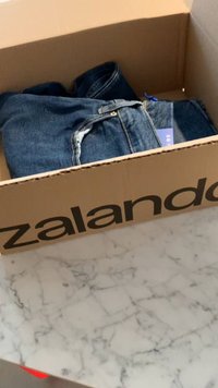 Džínsy v krabici Zalando, s tmavým praním, viditeľnými švami a štítkom s velikosťou, položené na mramorovom povrchu.