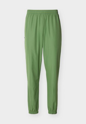 Rohelised spordipüksid, millel on elastne vöökoht ja soonikud all, külje peal väike logo, esitatud ühevärvilise tausta ees.