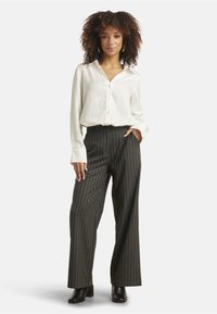 White button-up shirt, wide black pinstriped trousers, and black heeled boots. Smooth fabric with a relaxed fit and long sleeves.