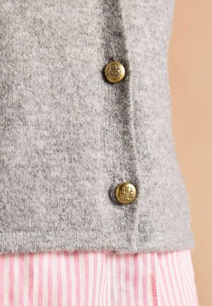 Grauer gestrickter Cardigan mit zwei goldenen Knöpfen, der eine weiche Textur zeigt. Pink gestreifter Stoff blitzt darunter hervor.