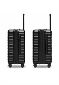 Deux valises rigides noires avec poignées télescopiques, quatre roues pivotantes, poignées latérales et serrures à combinaison TSA intégrées sur un fond blanc.