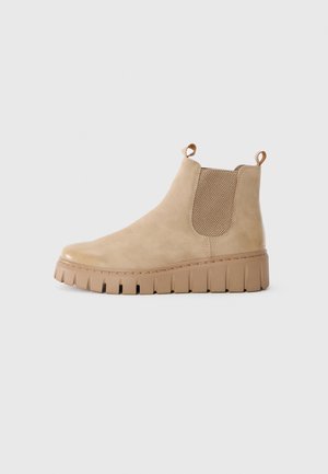 Botine Chelsea din suede bej, cu panouri laterale texturate, două bucle de tracțiune și o talpă din cauciuc masiv cu șanțuri distincte.