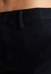 Black cotton trousers featuring a smooth texture, a simple waistband, and subtle stitching details. The fabric displays a matte finish.