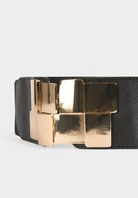 Cintura in pelle nera con una grande fibbia dorata lucida composta da forme quadrate e rettangolari sovrapposte.