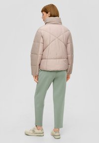 Wypchana, pastelowo-różowa kurtka z szarymi rękawami, wysokim kołnierzem oraz romboidalnym pikowaniem, zestawiona z jasnorozowymi spodniami i beżowymi trampkami.