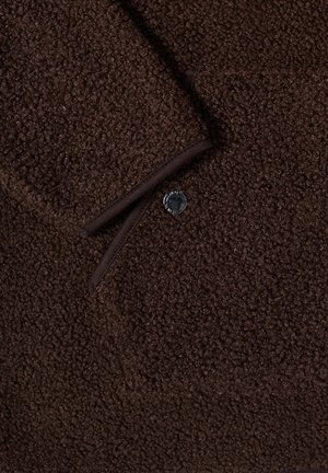 Tissu en laine texturé brun foncé avec un bouton noir et un poignet replié présentant des bords cousus.