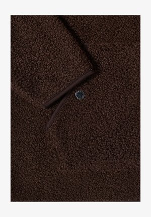 Tissu en laine texturé brun foncé avec un bouton noir et un poignet replié présentant des bords cousus.