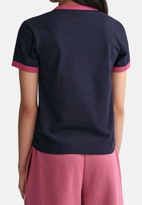 Camiseta de manga corta azul marino con ribete rosa alrededor del escote y las mangas. Fabricada con una tela suave y de corte relajado.