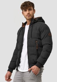 Schwarze Pufferjacke mit brauner Innenauskleidung, Reißverschluss vorne und strukturierter Oberfläche. Mit Seitentaschen und elastischen Bündchen.