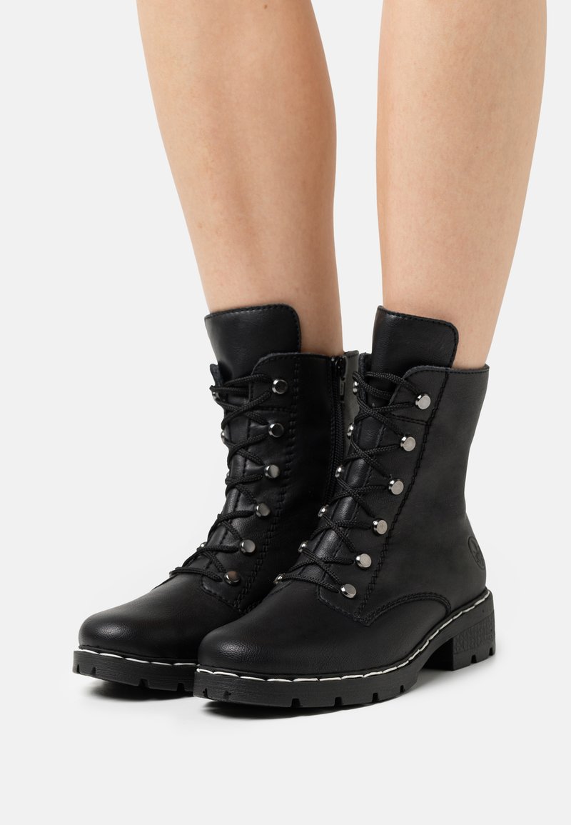 Bottines en cuir noir à lacets à l'avant, œillets métalliques, fermeture éclair sur le côté et semelle robuste avec des coutures blanches en accent.