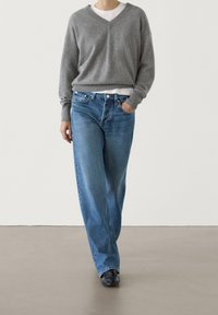 Gray knitted v-neck sweater and light blue loose-fitting denim jeans. The outfit is completed with black sneakers, accentuating a casual look.