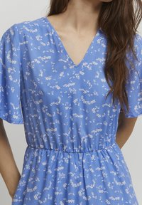 V-neck blue dress with short sleeves, featuring a subtle floral pattern in white. Elastic waistband provides a fitted silhouette.