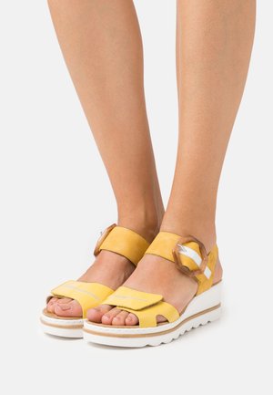 Gule lædersandaler med en hvid rem, justerbar ankelstropp og en tekstureret sål. Har syede detaljer og en dekorativ spænde.
