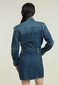Denim dress with long sleeves, dark blue color, fitted waist, and button cuffs. Features a cinched belt and a short length.