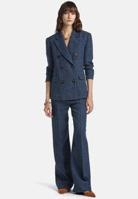 Blazer cruzado de mezclilla azul marino con grandes botones, pantalones de pierna ancha a juego y textura suave, combinado con zapatos de ante marrón.