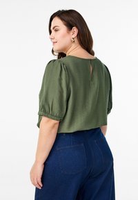 Blouse courte olive, à manches bouffantes et détail de trou de serrure dans le dos, associée à un pantalon taille haute bleu foncé avec poches arrière.