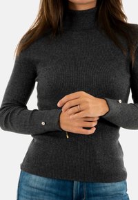 Maglione a costine grigio scuro aderente con collo alto, tessuto testurizzato e dettagli con bottoni sulle maniche. Indossato con jeans blu.