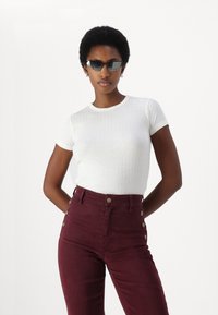 Top bianco a righe con maniche corte abbinato a pantaloni bordeaux a vita alta con dettagli a bottoni laterali. Texture liscia, design aderente.